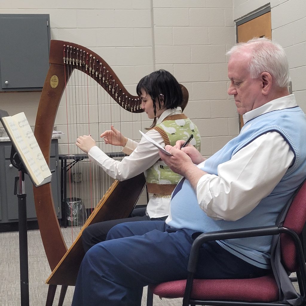 Teenage girl playing harp while teacher is taking notes