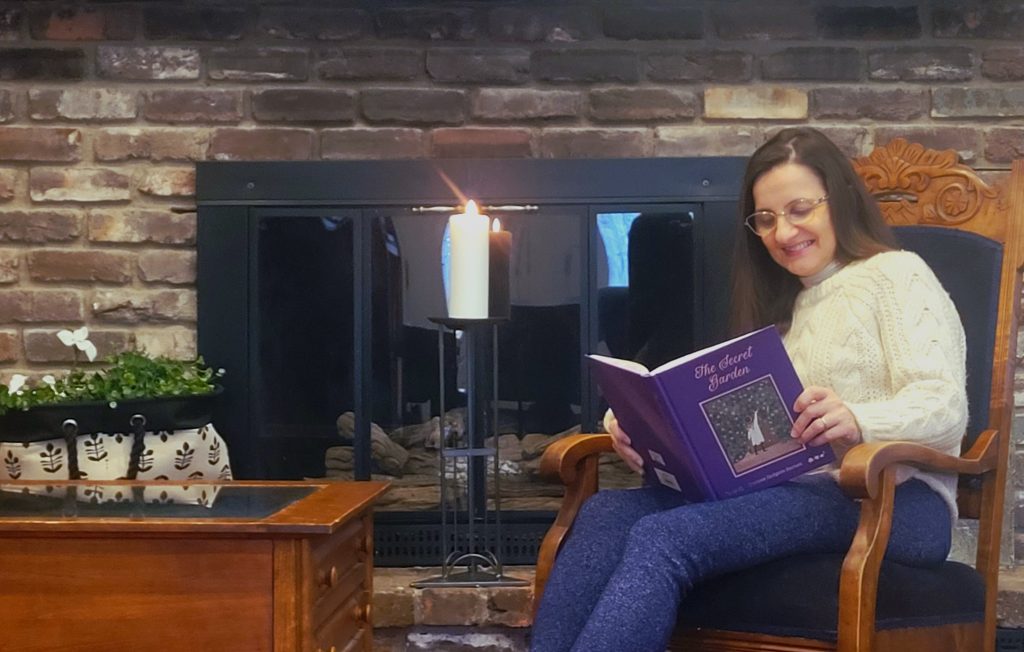 Woman reading The Secret Garden by the fireplace with a candle